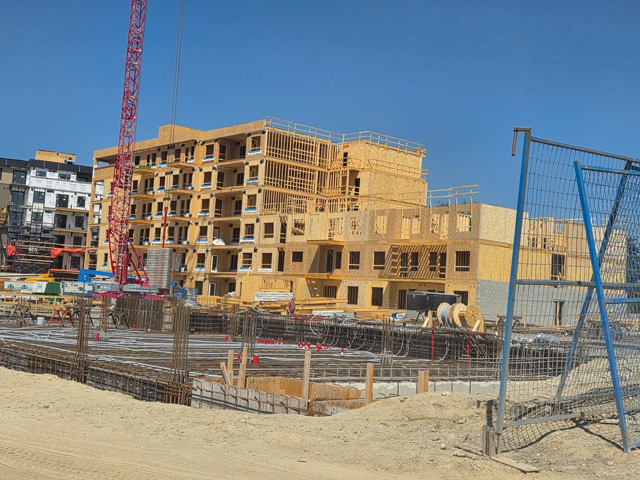 Wood-frame apartment building rising behind rebar foundation work