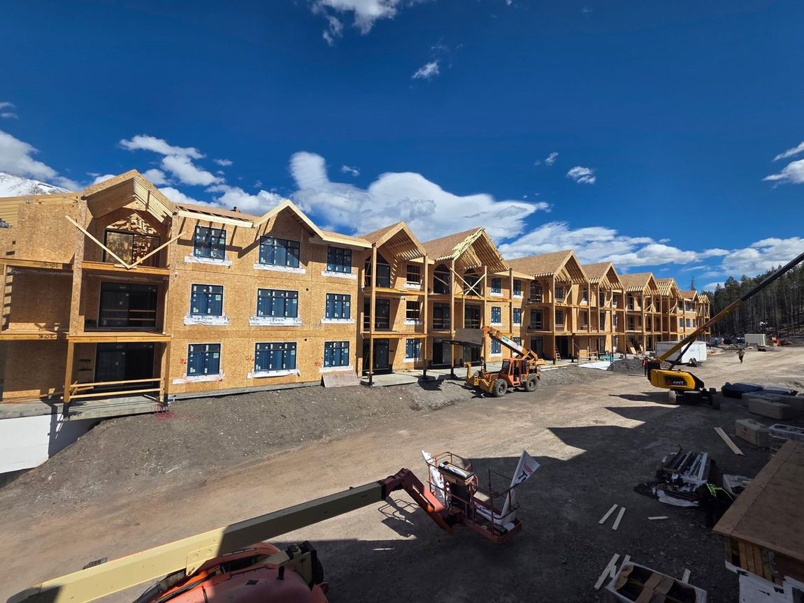 Wood-frame mountain resort buildings under construction with telehandlers on site